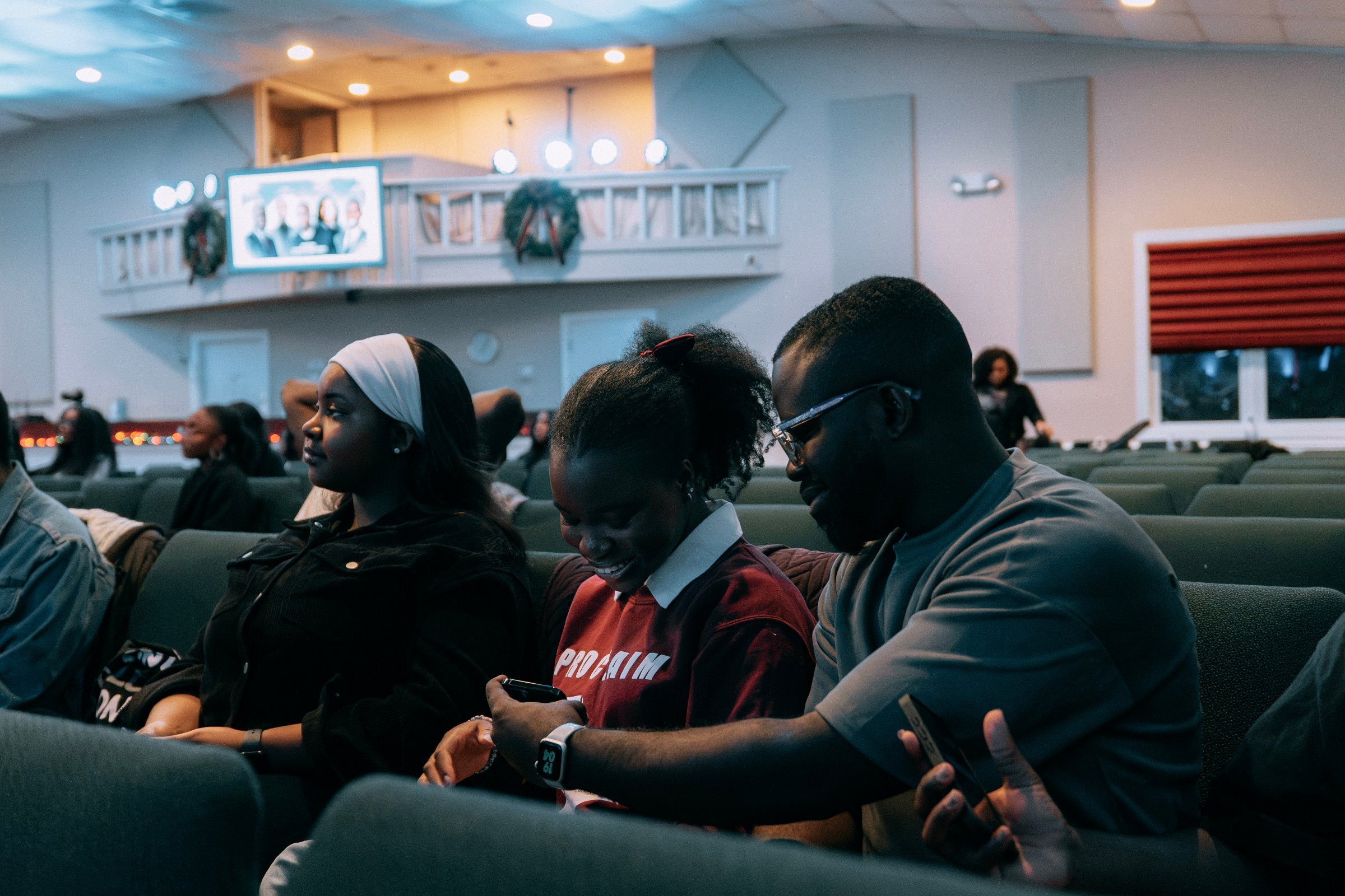 Three members of OneVoice sitting together in the pews, one laughing over a shared phone