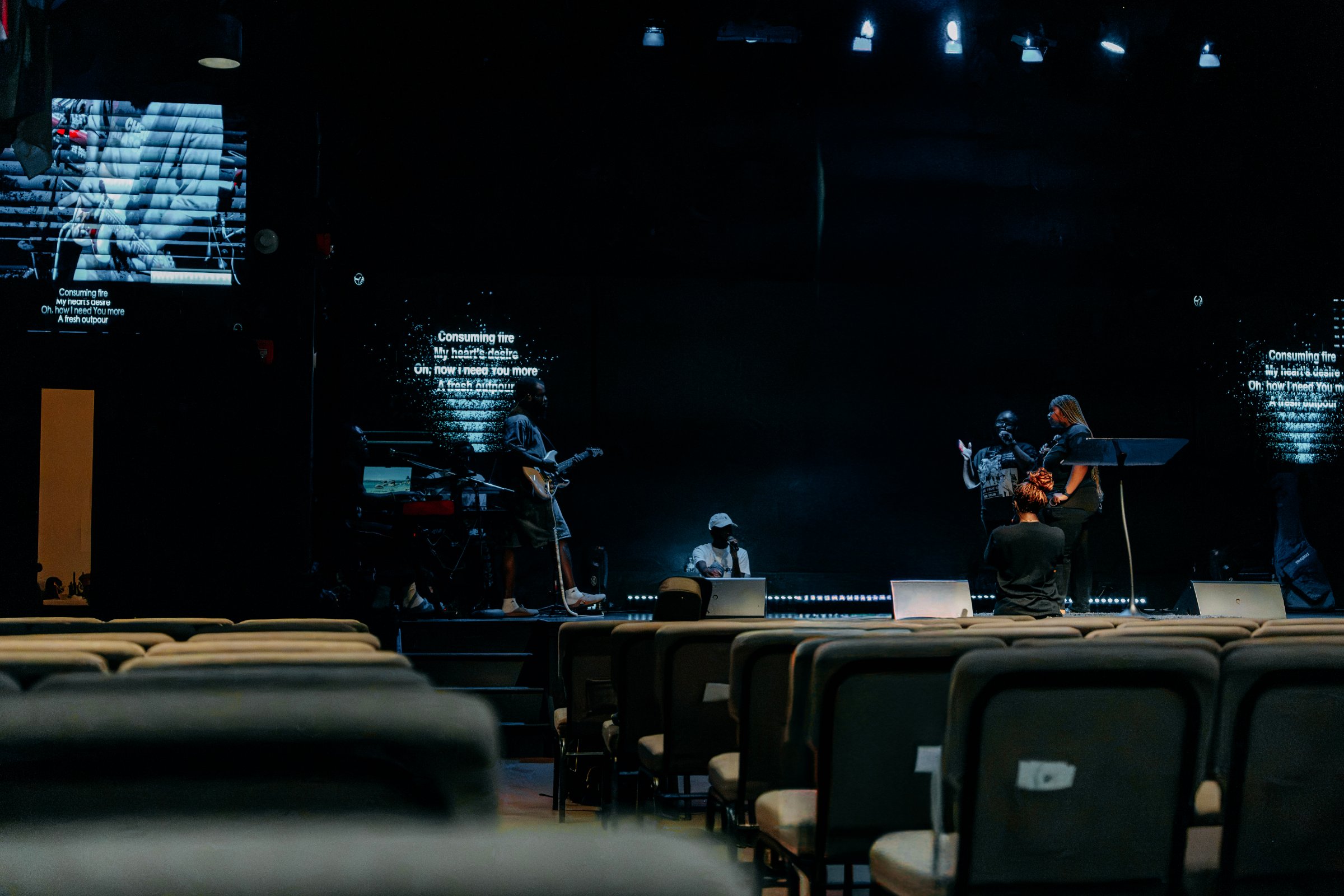 OneVoice rehearsing on stage, lyrics on the screens behind them
